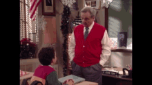 a man in a red vest is standing next to a boy in a classroom with the name george perry on the desk