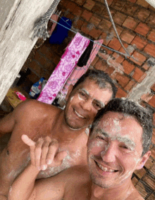 a man with soap on his face is standing next to another shirtless man