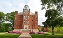 a large brick building with a clock tower on top of it is surrounded by trees and grass .