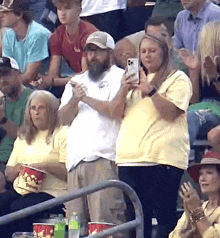 a group of people sitting in a stadium with buckets of popcorn and a man taking a picture with his phone