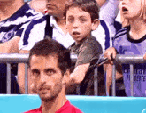 a young boy holds a tennis racquet in front of a man wearing a purple shirt that says fly better