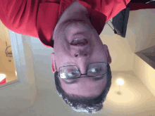 a man wearing glasses and a red shirt is looking upside down