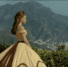 a woman in a yellow dress is walking in front of a mountain .