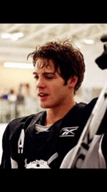 a young man wearing a hockey jersey is standing next to a hockey stick .