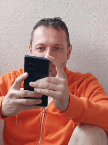 a man wearing an orange hoodie is looking at his cell phone