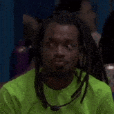 a man with dreadlocks is wearing a neon green shirt and making a face .