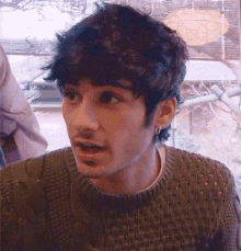 a young man wearing a green sweater and earrings is looking at the camera .