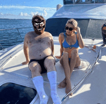 a woman in a bikini sits next to a man with a beard on a boat