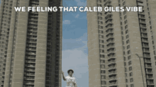 a man standing in front of tall buildings with the words " we feeling that caleb giles vibe " above him