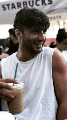 a man in a white tank top is holding a starbucks drink