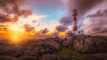 a red and white lighthouse sits on top of a rocky cliff at sunset