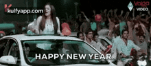 a woman is standing on the roof of a car holding balloons and a sign that says happy new year .