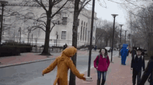 a woman in a red jacket is walking down a sidewalk with a man in a bear costume behind her