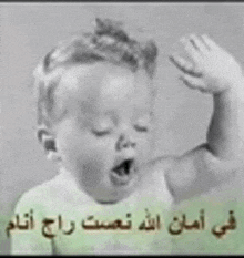 a black and white photo of a baby yawning with arabic writing on the bottom .