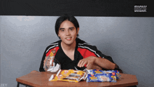 a young man sits at a table with a bag of candy and a bottle of water with snow break written on the bottom