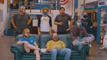 a group of people wearing masks are sitting on a couch in a room .