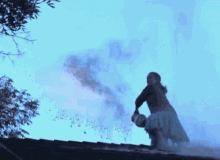 a woman is kneeling on the roof of a house with a bucket of smoke coming out of the chimney .