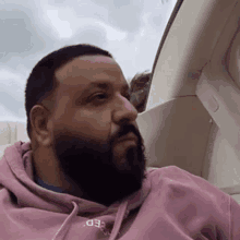 a man with a beard wearing a pink hoodie is sitting in a car looking out the window .