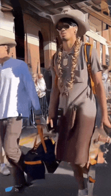 a man wearing a cowboy hat and sunglasses walks down the street