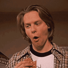 a man in a plaid shirt eating a waffle with his mouth open