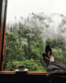 a person 's feet rest on a window sill with a cup of coffee on a saucer