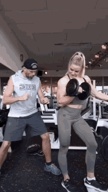 a man and a woman are lifting dumbbells in a gym with the man wearing a shirt that says boxing