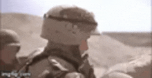 a soldier in a helmet is standing in the desert looking at something .