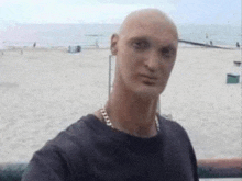 a bald man with a chain around his neck is standing on a beach .