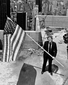 a man in a suit holds a large american flag