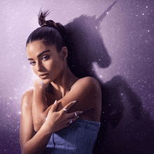 a woman with a ponytail stands in front of a purple background