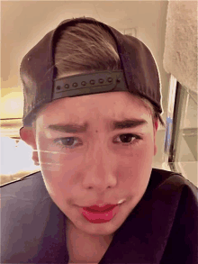 a young boy wearing a baseball cap and red lipstick