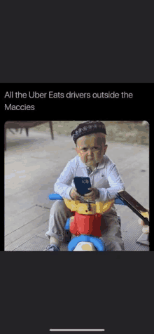 a baby is sitting on a toy horse holding a cell phone and looking at it .