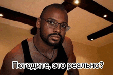 a man with glasses and a beard is wearing a black tank top and says " погодите " in russian