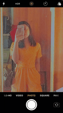 a woman in a yellow striped jumpsuit takes a selfie with her phone in front of a mirror