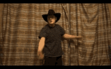 a man wearing a cowboy hat and striped shirt is standing in front of a curtain