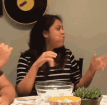 a woman in a striped shirt is sitting at a table with a bowl of food in front of her