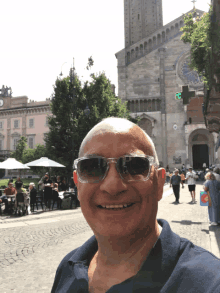 a man wearing sunglasses smiles in front of a building