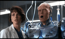 a woman in a lab coat stands next to a robot with its mouth open