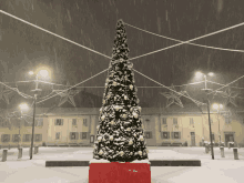 a christmas tree in front of a building with snow falling on it