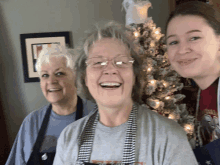 three women are posing for a picture in front of a christmas tree and smiling