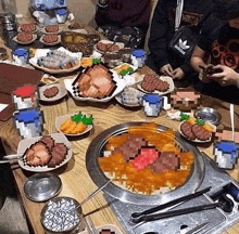 a group of people are sitting around a table with plates of food and a bowl of meat .