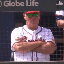 a man wearing sunglasses and a braves jersey stands with his arms crossed in front of a globe life sign