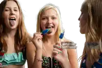 three young girls are sticking their tongues out and eating popsicles