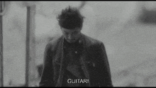 a black and white photo of a man walking down a street with the words `` guitar '' written on the bottom .