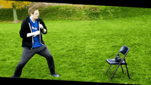 a man wearing a blue shirt that says nasa is standing next to a chair in a grassy field .