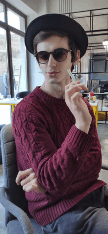 a man wearing sunglasses and a hat holds a cigarette in his hand