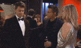 a man in a tuxedo with a bow tie is being helped by another man .