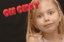 a little girl is making a funny face in front of a blackboard that says `` oh okay '' .