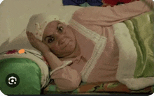 a woman in a pink shirt is laying on a bed with a green blanket