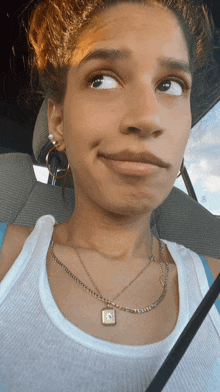 a woman wearing a white tank top and a gold necklace with a square pendant